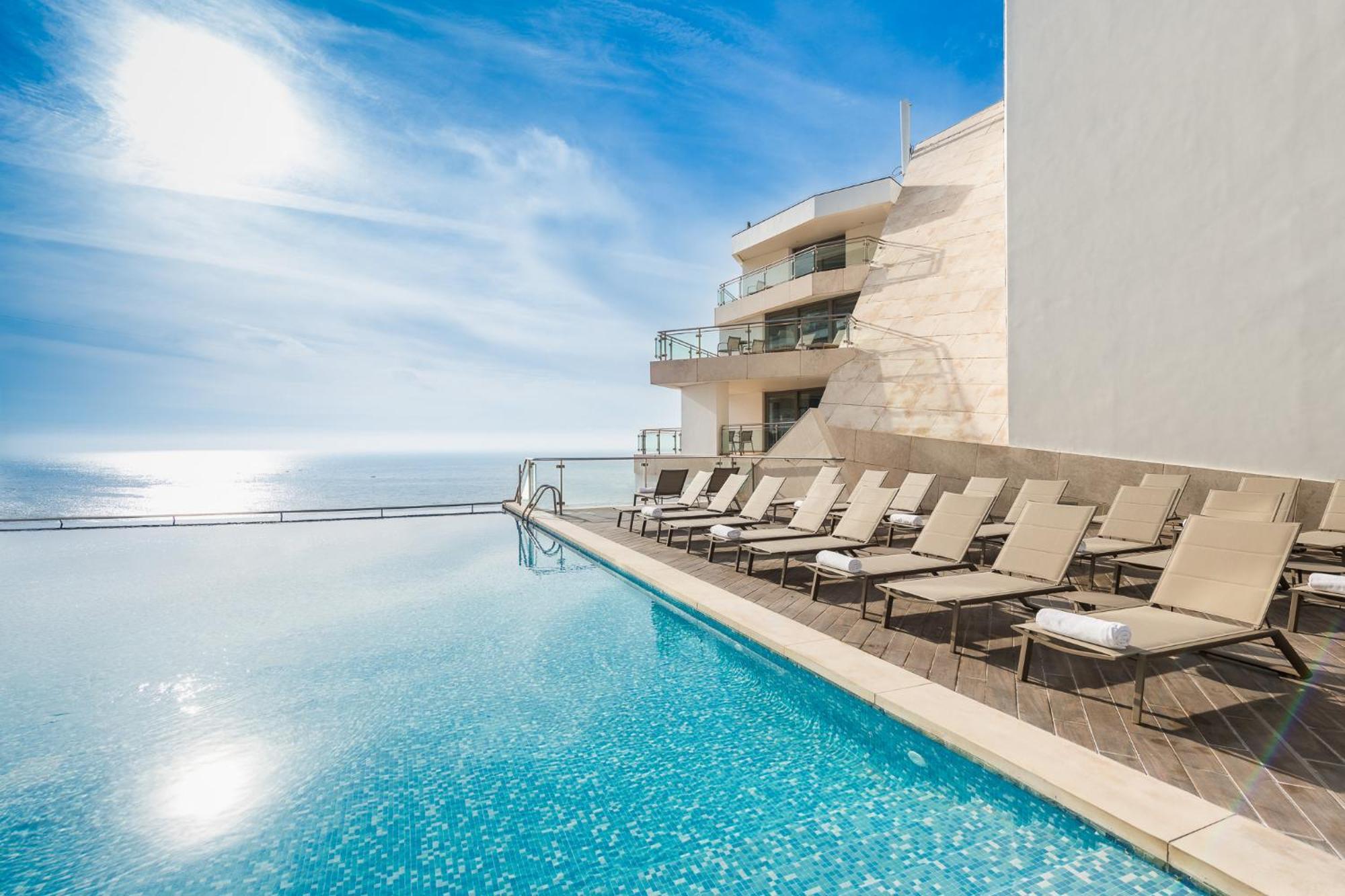 Sesimbra Hotel&Spa Exterior foto The photo showcases a luxurious infinity pool with crystal-clear water, reflecting the sky. Surrounding the pool are several sun loungers arranged neatly, inviting relaxation. In the background, there is a modern building with large glass balconies, 