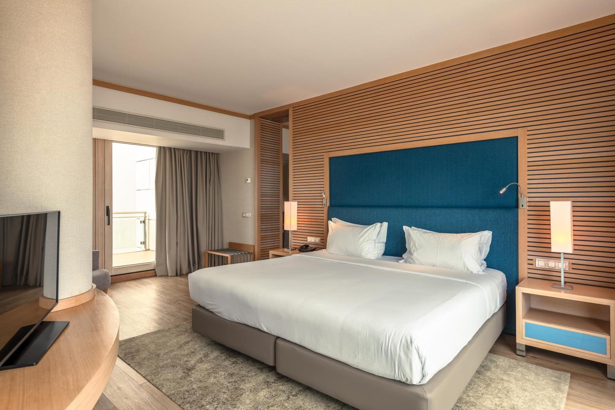 Sesimbra Hotel&Spa Exterior foto The photo shows a modern hotel room featuring a large bed with white bedding and a blue headboard. The room has light wood paneling and contemporary furnishings. There are bedside tables with lamps on either side of the bed, along with a circular rug