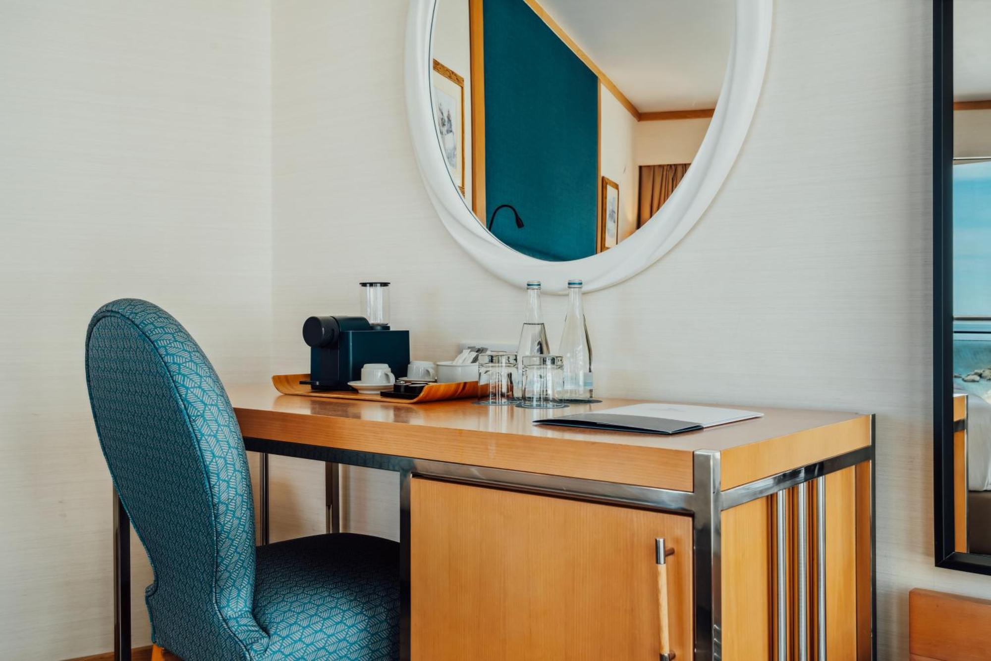 Sesimbra Hotel&Spa Exterior foto The photo shows a small workspace featuring a wooden desk and a padded chair in a teal color. On the desk, there are a few items: a vintage-style camera, a tray with glasses, and a notepad. Above the desk, there is a round mirror that reflects the ro